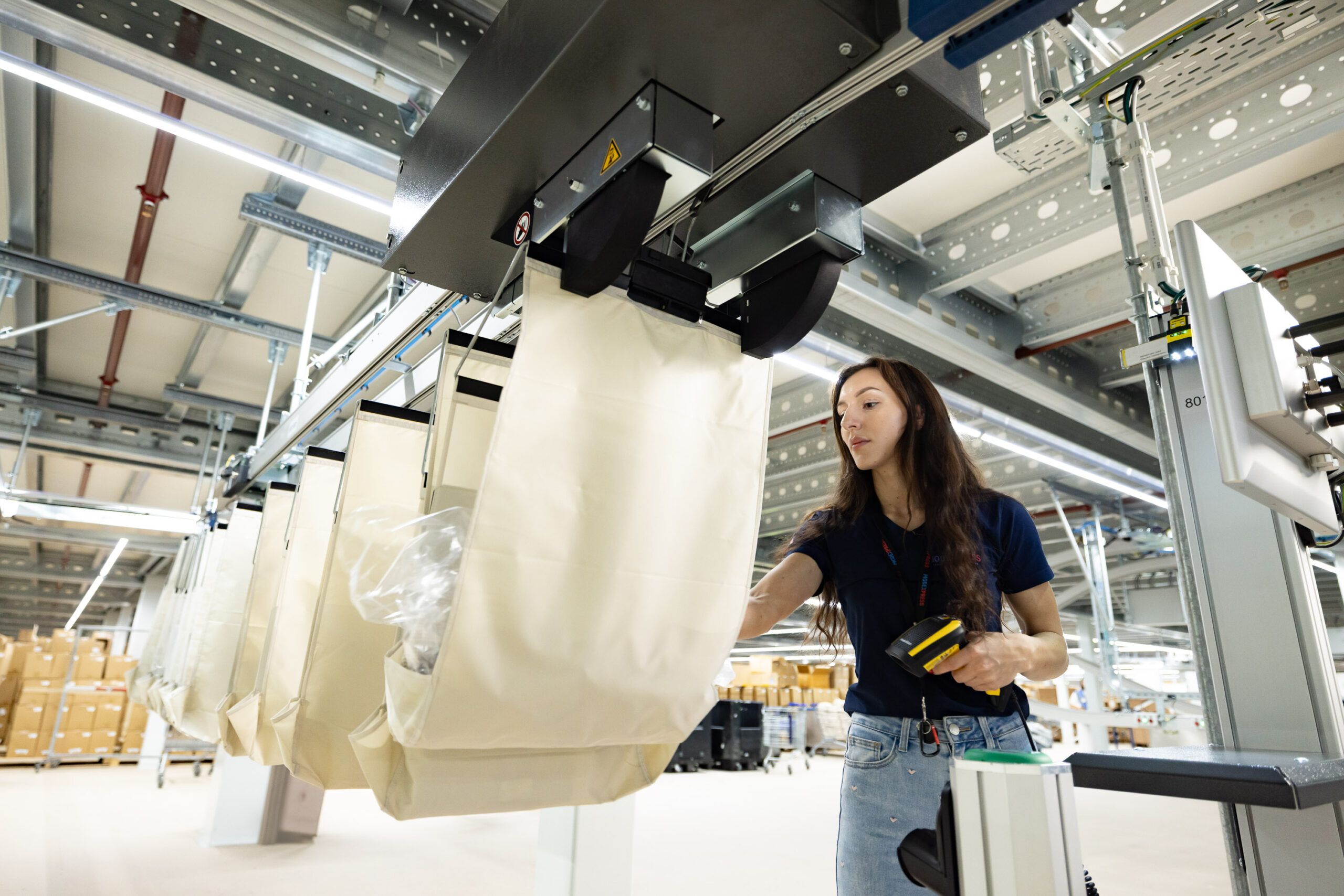 A woman scans items while working in a modern warehouse with automated storage containers above her.