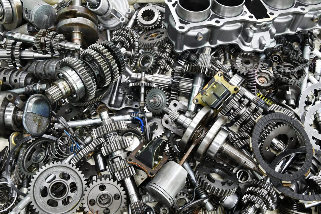 Ein großer Stapel verschiedener Metallzahnräder, Kolben, Stangen und anderer mechanischer Motorenteile, die dicht aneinandergereiht sind und die komplizierten Komponenten von Industriemaschinen zeigen, die für die Ersatzteillogistik im Maschinenbau unerlässlich sind.