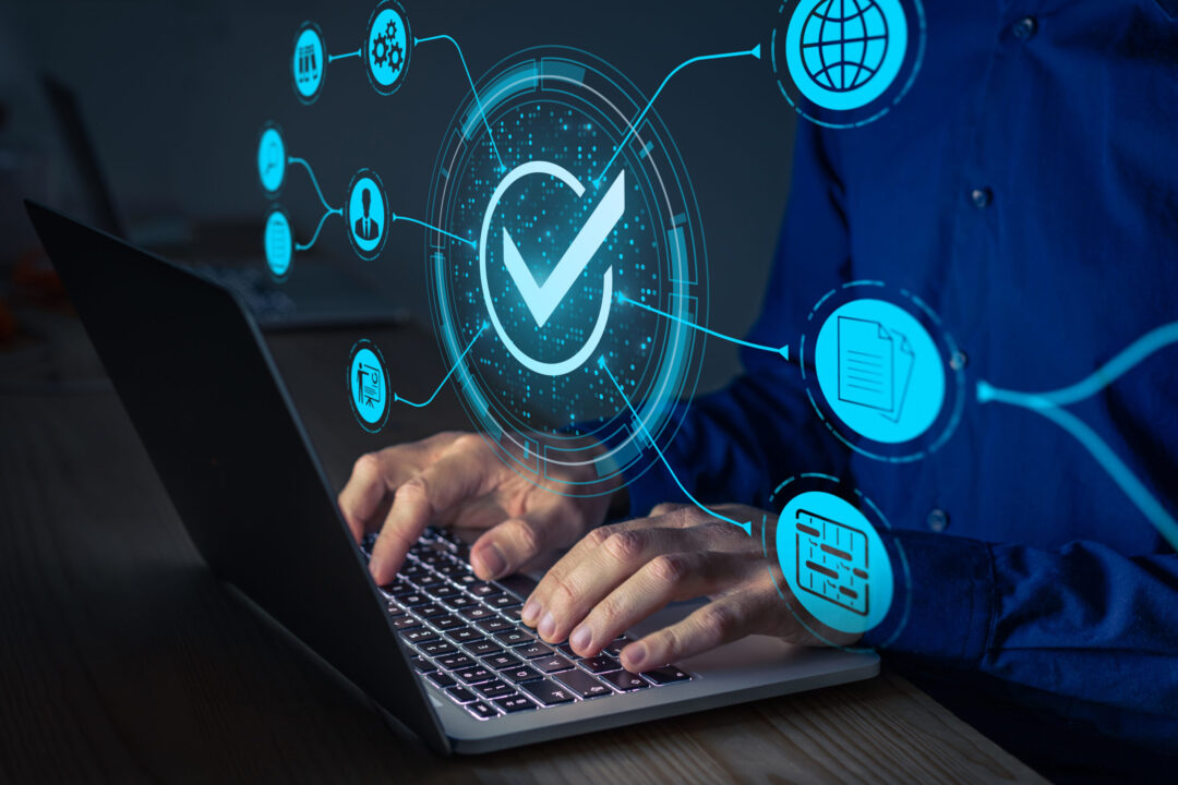 Eine Person tippt auf einem Laptop. Digitale Symbole um ein großes Häkchen repräsentieren Konzepte wie Sicherheit, Servicemanagement, Internet und Online-Verifizierung. Das Bild vermittelt einen futuristischen, technologischen Eindruck.