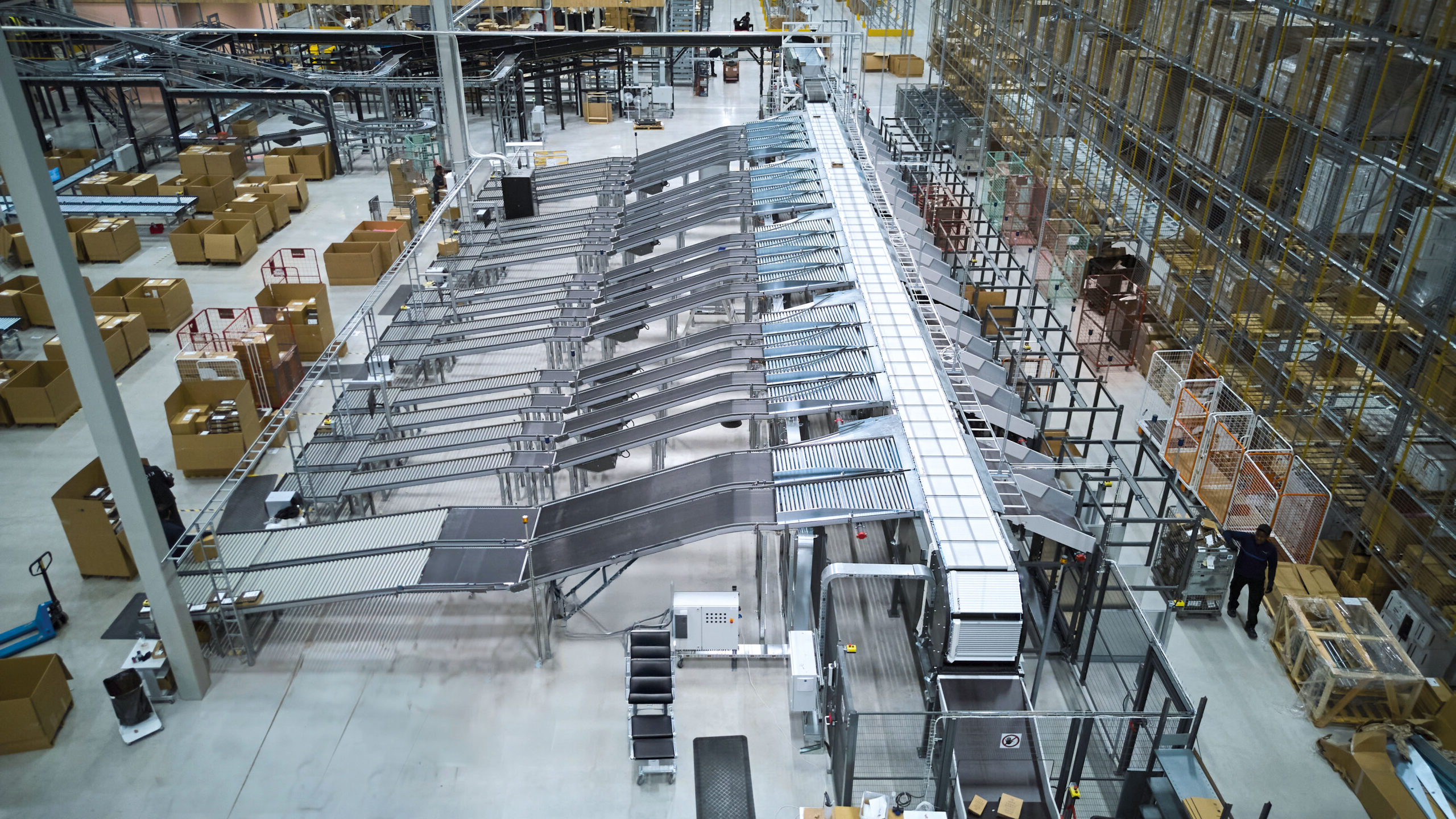 Luftaufnahme eines modernen Lagerhauses mit Förderbändern, Sortiermaschinen, Metallregalen und verstreuten Kartons, die ein geschäftiges automatisiertes Vertriebs- oder Fulfillment-Zentrum darstellen.